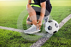 Soccer ball on green artificial turf with footballer is sitting and catch the ankle