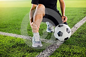 Soccer ball on green artificial turf with footballer is sitting and catch the ankle