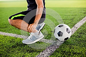 Soccer ball on green artificial turf with footballer is sitting and catch the ankle