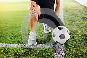 Soccer ball on green artificial turf with footballer is sitting and catch the knee