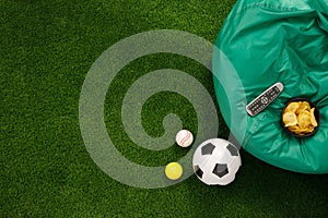 Soccer ball on a green field and ottoman for a fan with snacks and a TV remote control. The apartment was lying. The concept of