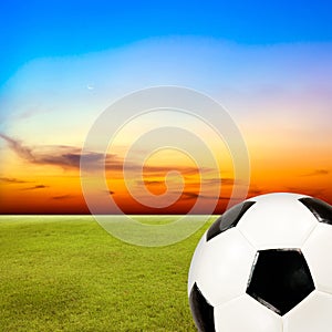 Soccer ball with green grass field against sunset sky