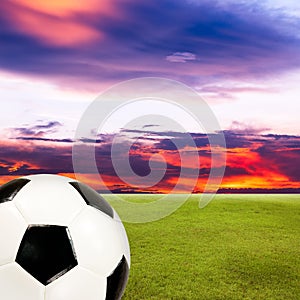Soccer ball with green grass field against sunset sky