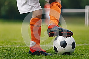 Soccer ball kick. Close up of legs and feet of football player in red socks and cleats running and dribbling with the ball