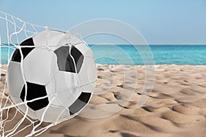 Soccer ball in net on sandy coast near sea. Beach football