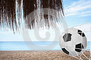 Soccer ball in net on sandy coast near sea. Beach football