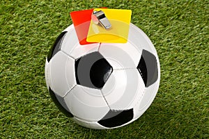 Soccer ball with referee yellow and red cards and chrome whistle on top over grass background - penalty, foul or sports concept