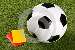 Soccer ball with referee yellow and red cards on grass background - penalty, foul or sports concept