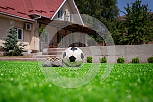 Soccer ball and shoes on the lawn against the background of house with terrace. Home football concept