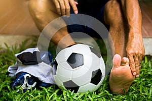 Soccer ball and sport shoes on green grass with soccer player catch the ankle of the feet because of pain