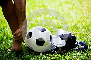 Soccer ball and sport shoes on green grass with soccer player catch the ankle of the feet because of pain