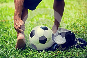 Soccer ball and sport shoes on green grass with soccer player catch the ankle of the feet because of pain