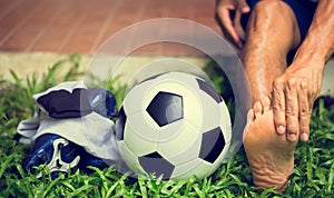 Soccer ball and sport shoes on green grass with soccer player in foot  pain