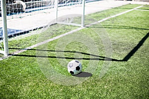 Soccer ball with sunlight and shadow on green field in front of goal post