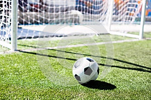 Soccer ball with sunlight and shadow on green field in front of goal post