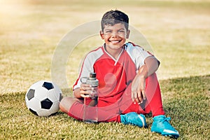 Soccer, children and water with a ball and boy child sitting on a grass pitch or field after training. Football, fitness