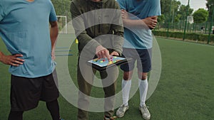 Soccer coach explaining match tactics to football players outdoors