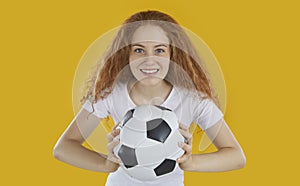Soccer fan happy smiling readhead woman holding football ball in hands on yellow background.