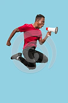 Soccer fan jumping on blue background. The young afro man as football fan with megaphone