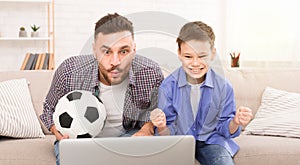 Soccer fans dad and son watching soccer match on laptop online