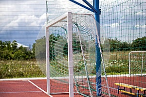 Soccer or football field playground with bright red soft rubber flooring, big gate, empty bench and protective net fence in rural