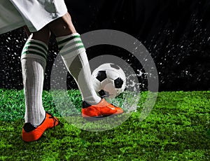 Soccer football players kicking to soccer ball on green grass field with splashing of transparent water against black background