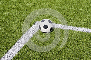 The soccer football on the white line in the artificial green grass field