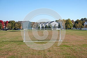 Soccer goal net on a field with green and grown grass near houses with no people present