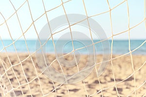 Soccer goal net on summer beach background. Focus on the grid on the background of blurry sandy shore.