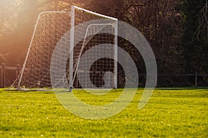 Soccer goal post in a green field, Selective focus, Warm sunny day, Sun flare, dark trees in the background. Concept football