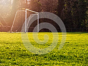 Soccer goal post in a green field, Selective focus, Warm sunny day, Sun flare, dark trees in the background. Concept football