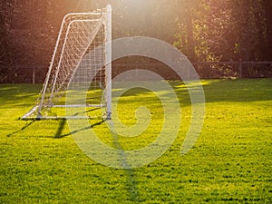 Soccer goal post in a green field, Selective focus, warm sunny day, Sun flare, dark trees in the background. Concept football