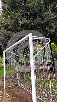 Soccer net in a public park with mud and puddles and trees in the background on a cloudy day
