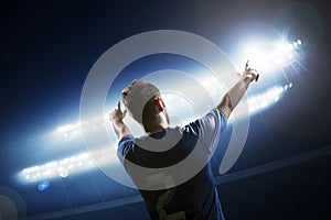 Soccer player with arms raised cheering, stadium at night time