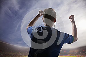 Soccer player with arms raised cheering, stadium with sky and clouds