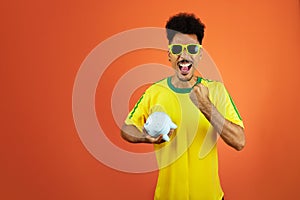 Soccer Player - Black Man Celebrating Holding Pig Coin Isolated on Orange Background