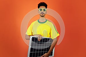 Soccer Player - Black Man Celebrating Holding Solar Photovoltaic Panel Isolated on Orange Background