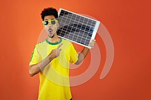 Soccer Player - Black Man Celebrating Holding Solar Photovoltaic Panel Isolated on Orange Background