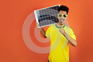 Soccer Player - Black Man Celebrating Holding Solar Photovoltaic Panel Isolated on Orange Background