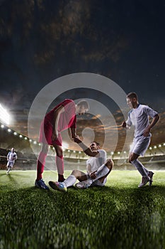 Soccer player helps onother one on sunset stadium background panorama