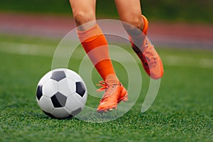 The soccer player hits the ball on the artificial turf. Footballer in sports cleats kicking a ball