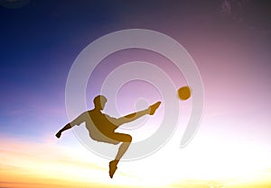 Soccer player kicks ball with sunset background