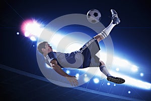 Soccer player in mid air kicking the soccer ball, stadium lights at night in background