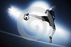 Soccer player in mid air kicking the soccer ball, stadium lights at night in background