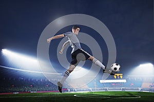 Soccer player in mid air kicking the soccer ball, stadium lights at night in background