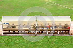 Soccer players and staff sit on bench beside the soccer field. (Home team)