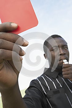 Soccer referee holding out red card and whistle