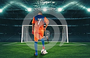 Soccer scene at night match with player in orange uniform kicking the penalty kick