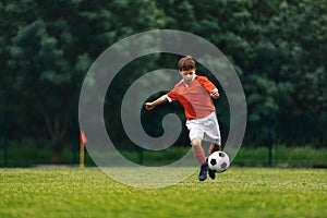Soccer shooting. Boy kicking soccer ball on grass field. Young football player in action running jumping, and shooting the ball