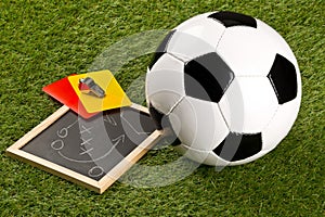 Soccer sports ball and referee chrome whistle with game strategy drawing blackboard and yellow and red referee cards on grass